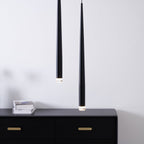 Two black tapered pendants close to the camera above a black chest with brass handles and a stack of books, from Clérachic.