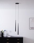 Two black tapered pendants hang above a black chest, with a vase of flowers and a framed print on the wall, a Clérachic pendant.