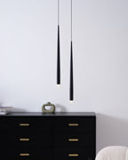 Pair of black cone pendants in front of a pale wall, a black chest below with a small sculptural vase, from Clérachic.