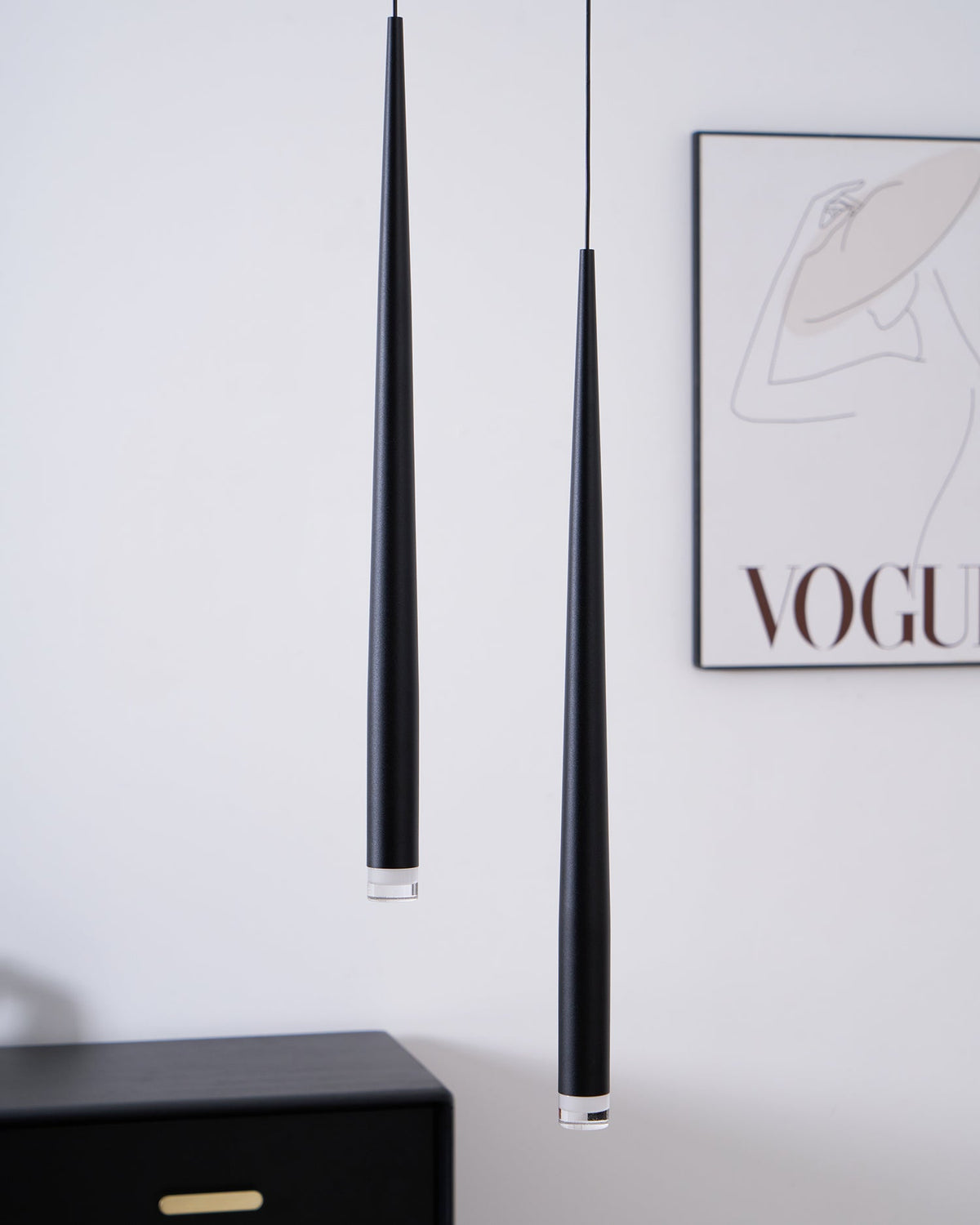 Close view of two black tapered pendants beside a framed line-art print and a black chest, from Clérachic.