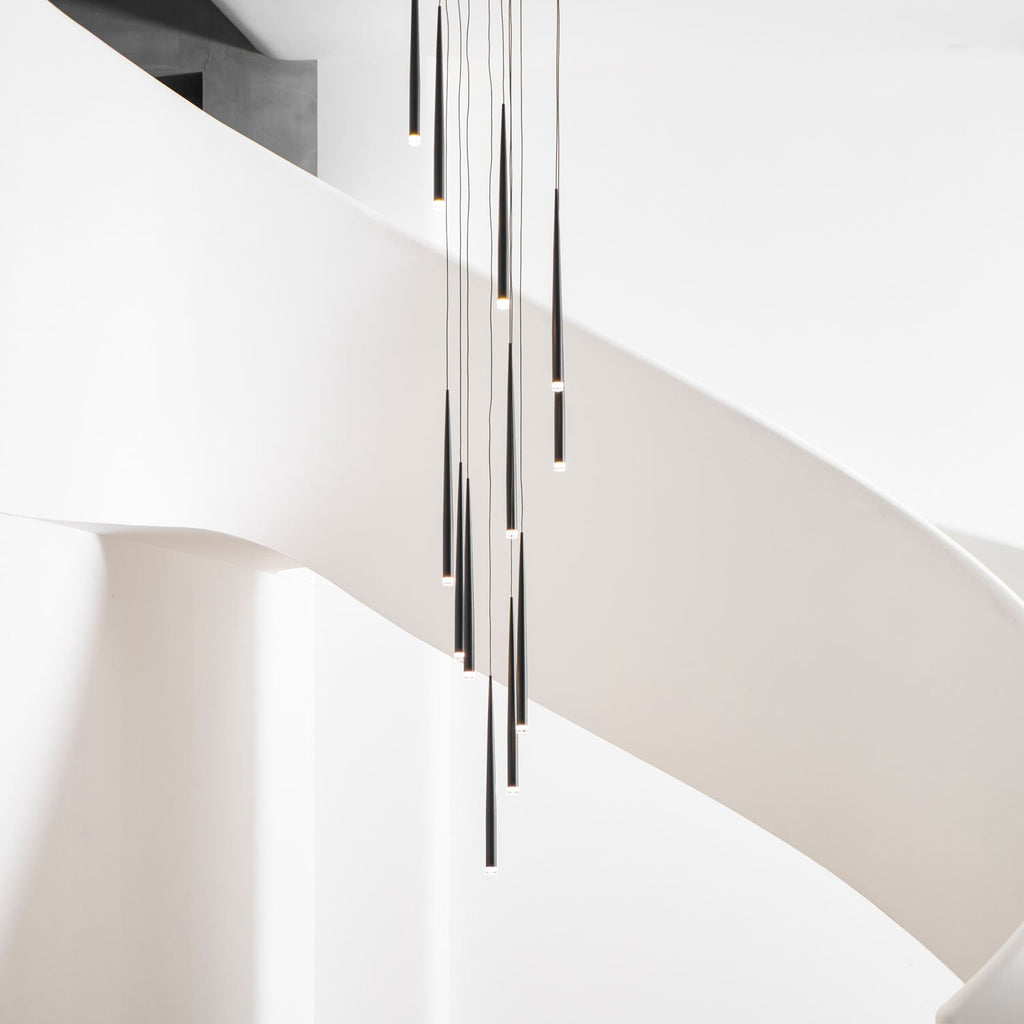 Black needle pendants hang in front of a sweeping white spiral staircase, cropped tight on the lower tips, a Clérachic pendant.