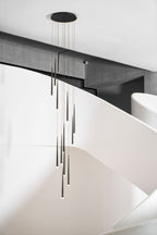 Round-canopy cluster of black tapered pendants hangs by a curving white staircase with a dark beam above, from Clérachic.