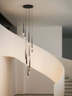Warm light on a white spiral staircase as a Clérachic pendant cluster glows beneath its round black canopy.