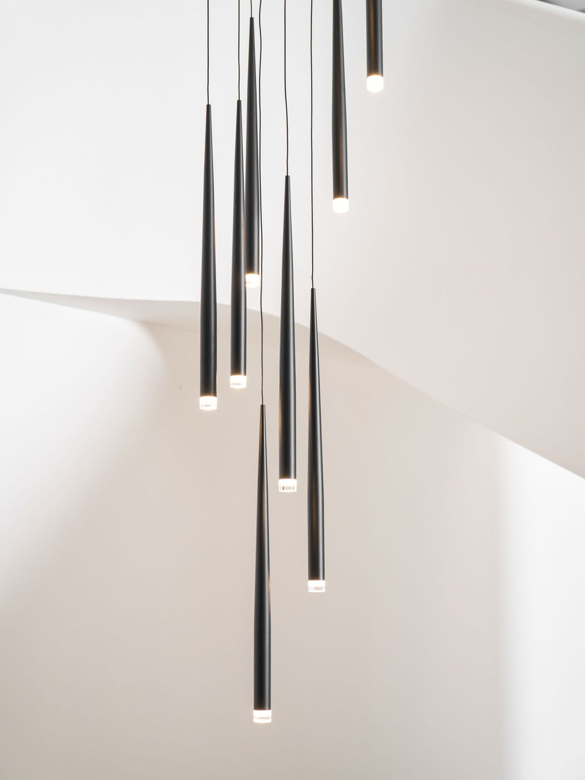 Close, cropped view of lit black cone pendants against a white curved stair wall, tips glowing, a Clérachic pendant.