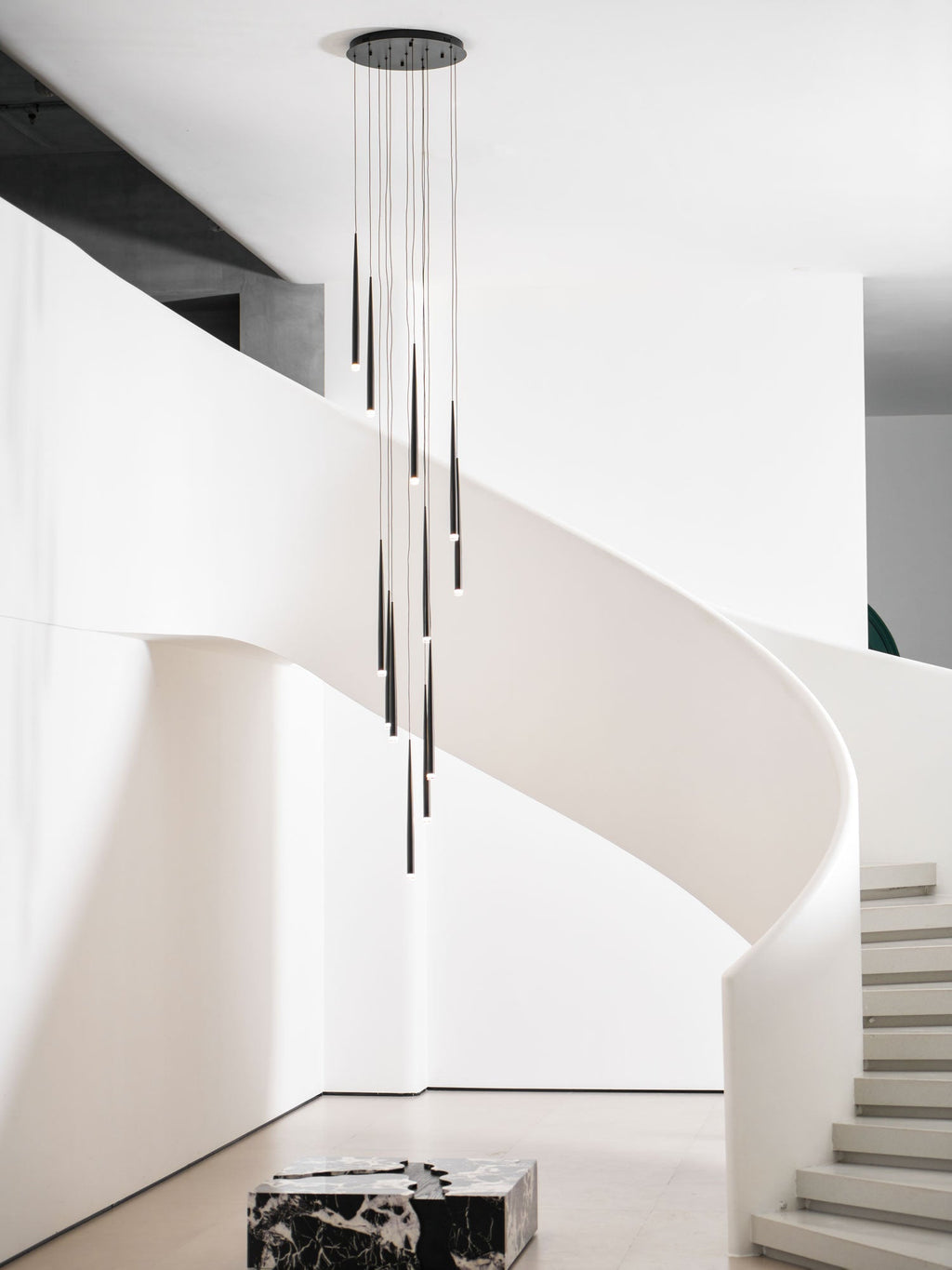 Tall view of this Clérachic pendant cluster in a white stair hall, with steps and a marble block at the base.