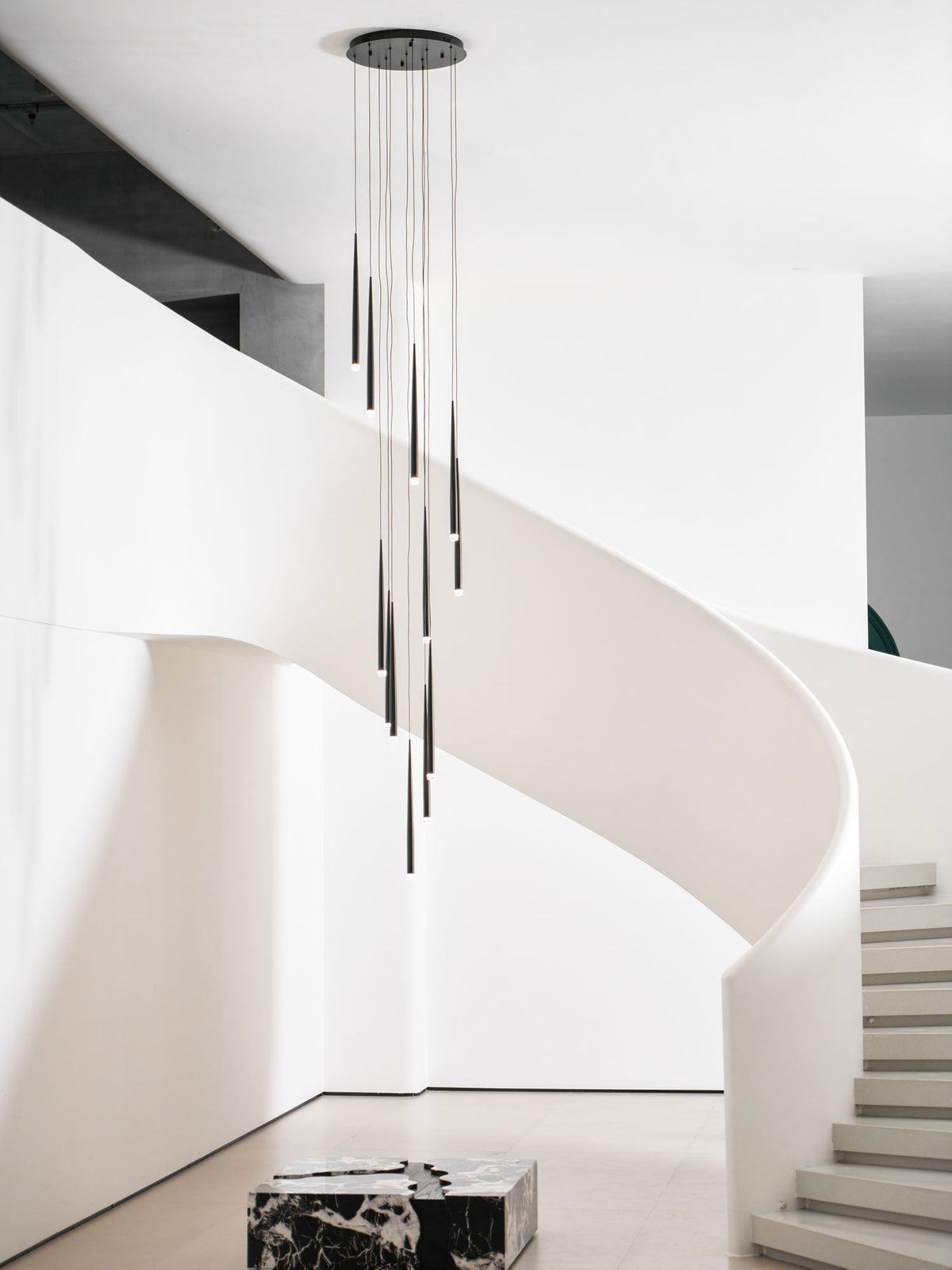 Tall view of this Clérachic pendant cluster in a white stair hall, with steps and a marble block at the base.