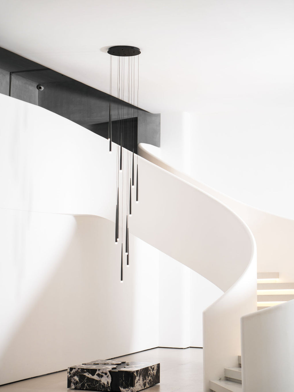 Pendant cluster hangs from a round black canopy by a white spiral staircase and a marble block, a Clérachic pendant.