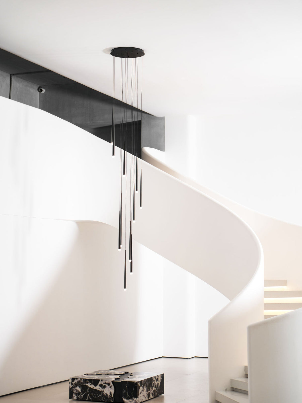 Pendant cluster hangs from a round black canopy by a white spiral staircase and a marble block, a Clérachic pendant.