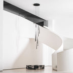 Wide room view with a white spiral stair and a dark beam, the black tapered pendants hanging in the centre, from Clérachic.