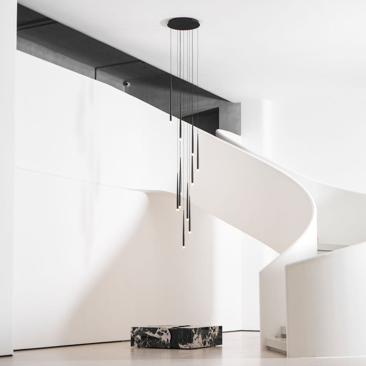 Wide room view with a white spiral stair and a dark beam, the black tapered pendants hanging in the centre, from Clérachic.