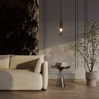 The black-tinted pendant lights a bronze side table stacked with books beside a cream sofa and stone feature wall, Clérachic lifestyle shot.