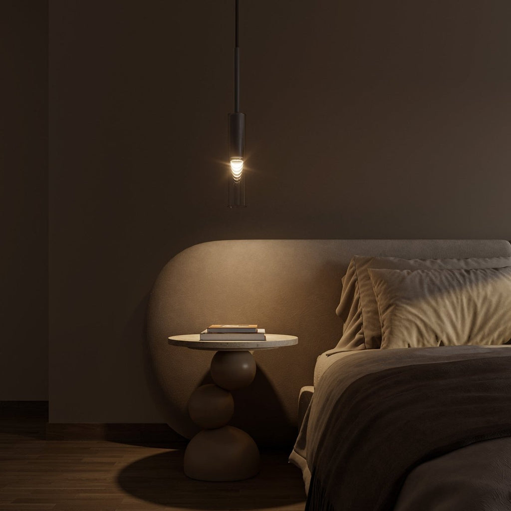 A single black-tinted pendant glows warm above a round nightstand beside a curved upholstered headboard, Clérachic lifestyle shot.