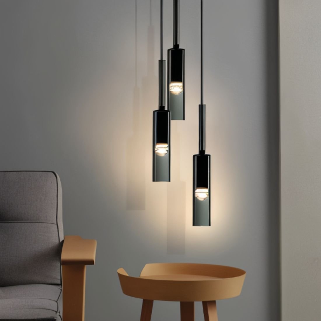 Three clustered black-tinted pendants hang above a round wooden stool beside a grey armchair in this Clérachic lifestyle shot.