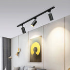 Clérachic black track with three black cylindrical spotlights angled down, lighting a wall with a yellow-and-black artwork.