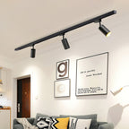 Clérachic black track with three black cylindrical heads above a living room wall with framed prints and a grey sofa.