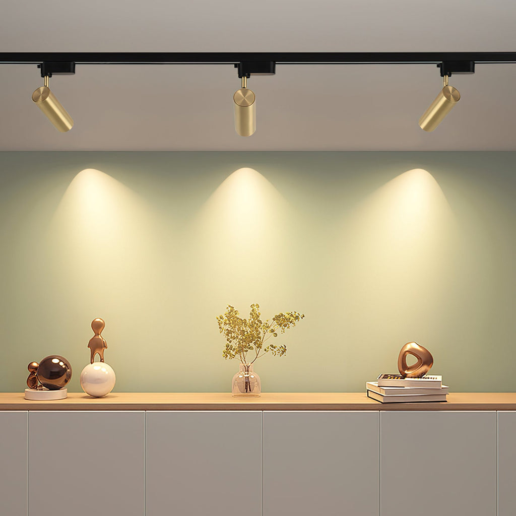 Three gold cylindrical Clérachic track heads, each lighting a soft pool of warm light on a green wall above a sideboard.