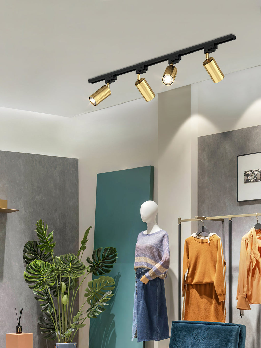 Gold-headed Clérachic track spotlights over a clothes shop display, with a mannequin, a rail of orange clothes and a plant.