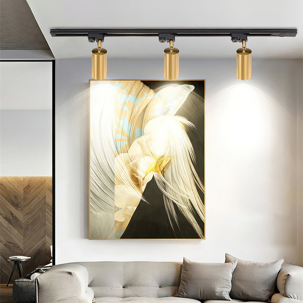 Three gold Clérachic track heads lighting a large framed feather artwork above a grey sofa.