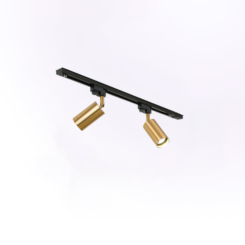 Two gold cylindrical Clérachic spotlights on a black track seen at an angle, on a soft white background.