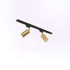 Two gold cylindrical Clérachic spotlights on a black track seen at an angle, on a soft white background.