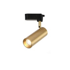 Gold cylindrical Clérachic track spotlight with a black adaptor, shown from below to show its honeycomb lens.