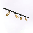 Four gold Clérachic spotlights on an angled black track, each head tilted differently, on a pale backdrop.