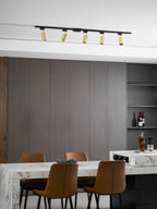 Distant view of a Clérachic track with five gold spotlight heads on a white ceiling, above a marble table and leather chairs.