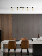 Clérachic gold-headed track along a white ceiling in a dining room with dark panelling, a marble island and tan chairs.