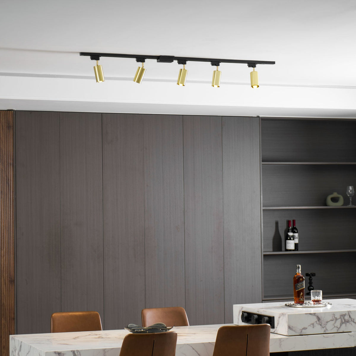 Five gold Clérachic spotlights on a track near the ceiling, with dark wall panels and shelves holding wine bottles.