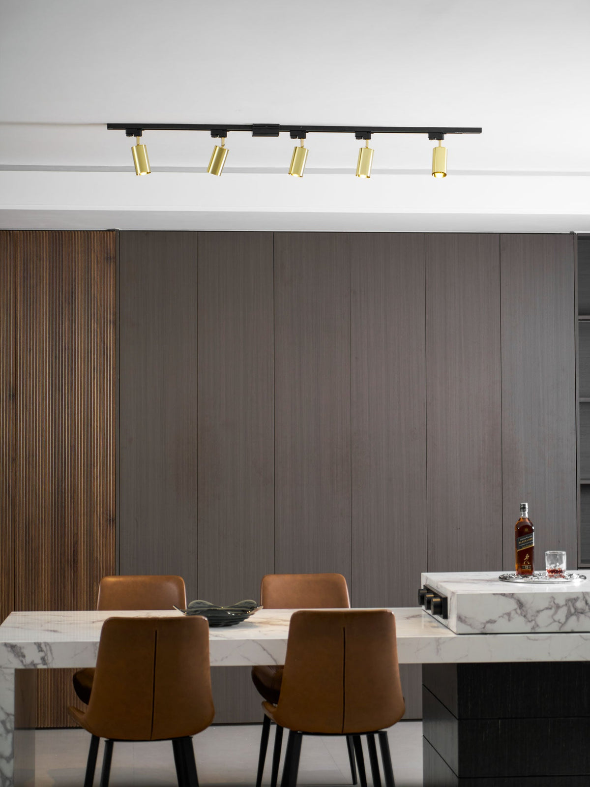 Clérachic track with five gold spotlights over a wooden-panelled dining area with a marble table and leather chairs.