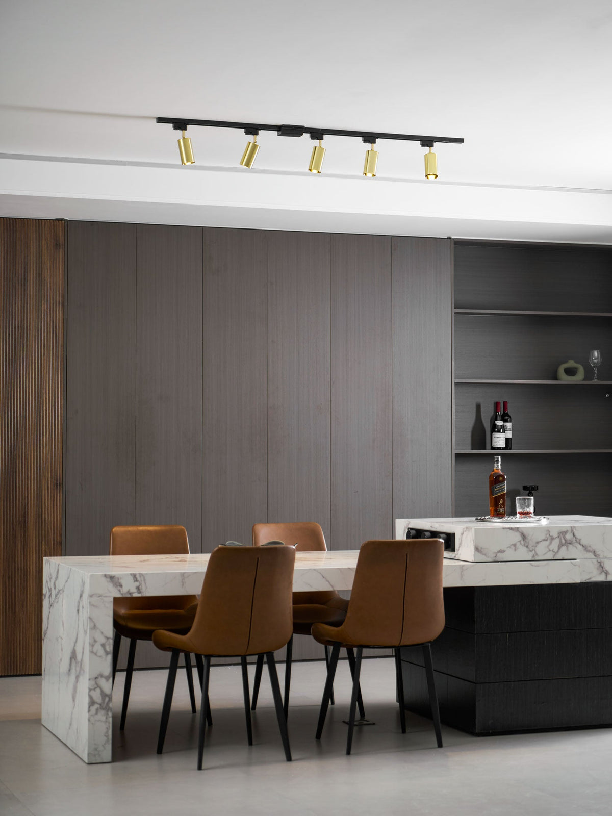 Wide room view with a Clérachic five-head gold track light, a marble island, tan chairs and a grey panelled wall.