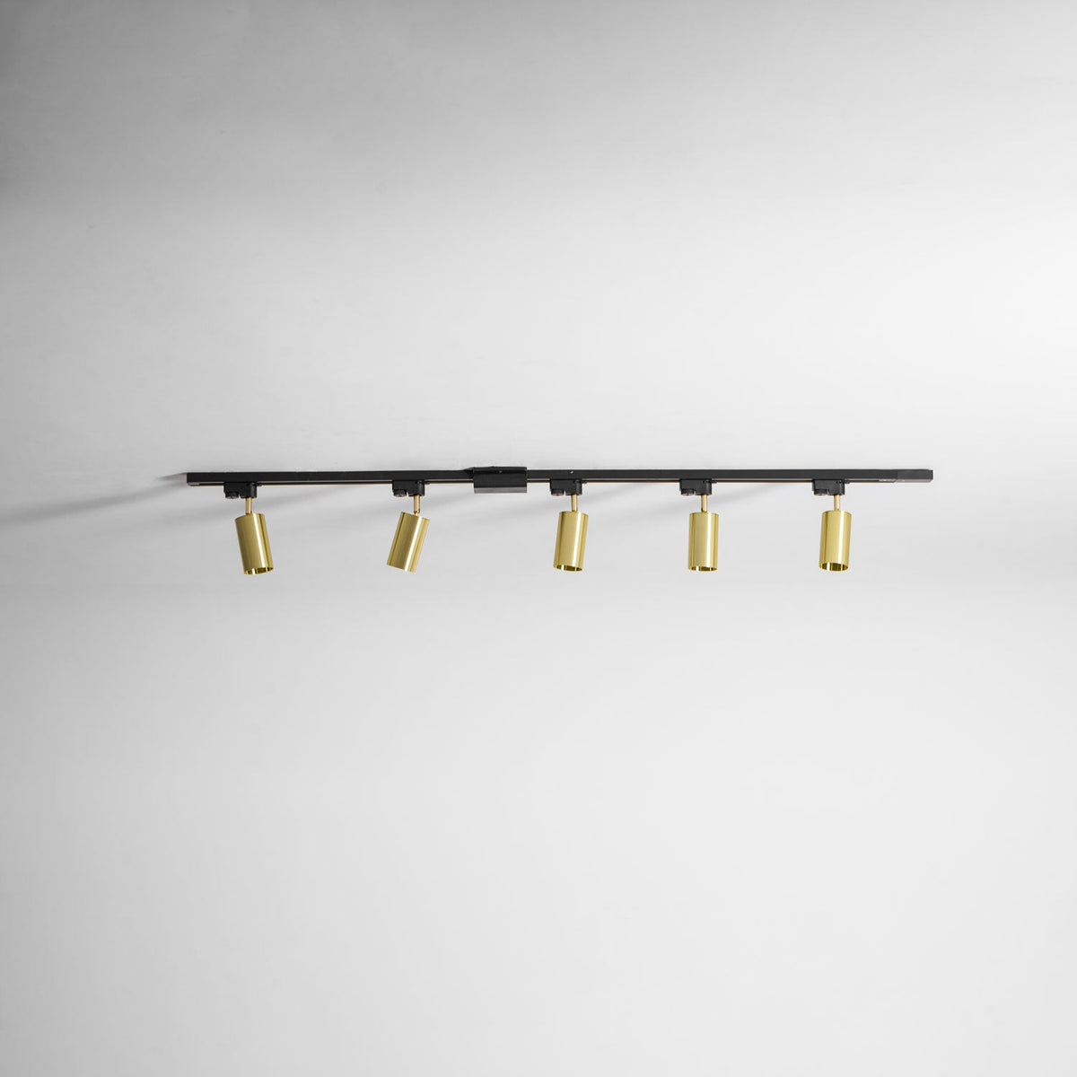 Clérachic black track with five gold cylindrical spotlights, seen along a plain white ceiling.