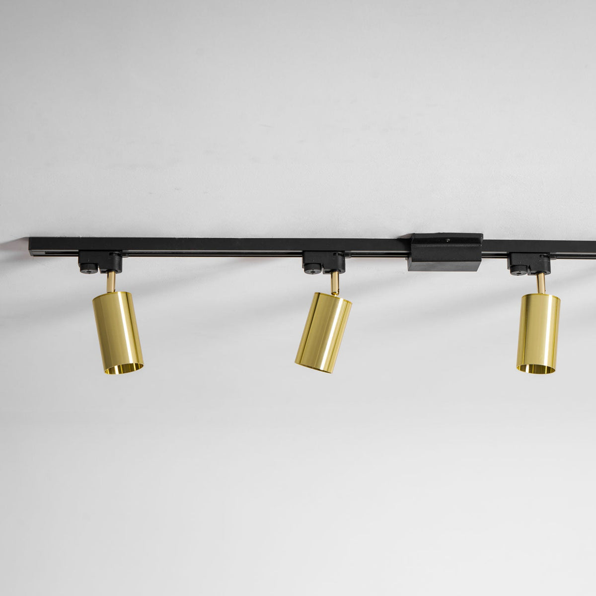 Three gold Clérachic spotlights on a black track with a joining piece, angled down from a white ceiling.