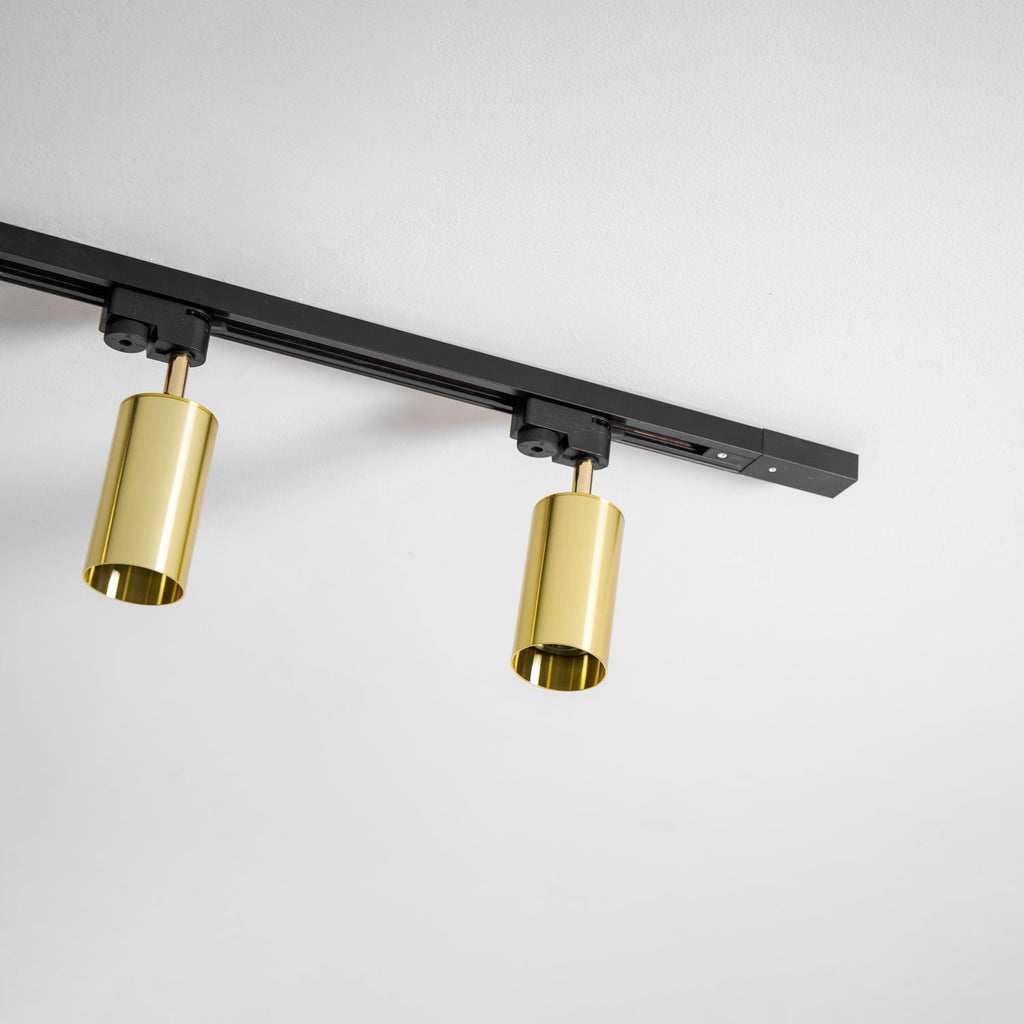 Two polished gold Clérachic spotlights on an angled black track, seen from below against a white ceiling.