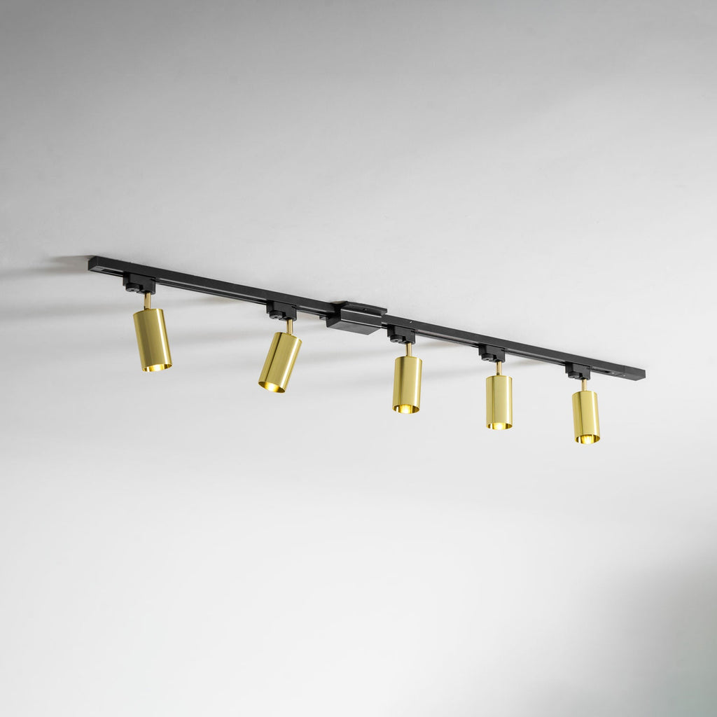 Five gold Clérachic spotlights on a black track, seen at an angle along a white wall and ceiling.