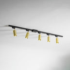 Five gold Clérachic spotlights on a black track, seen at an angle along a white wall and ceiling.