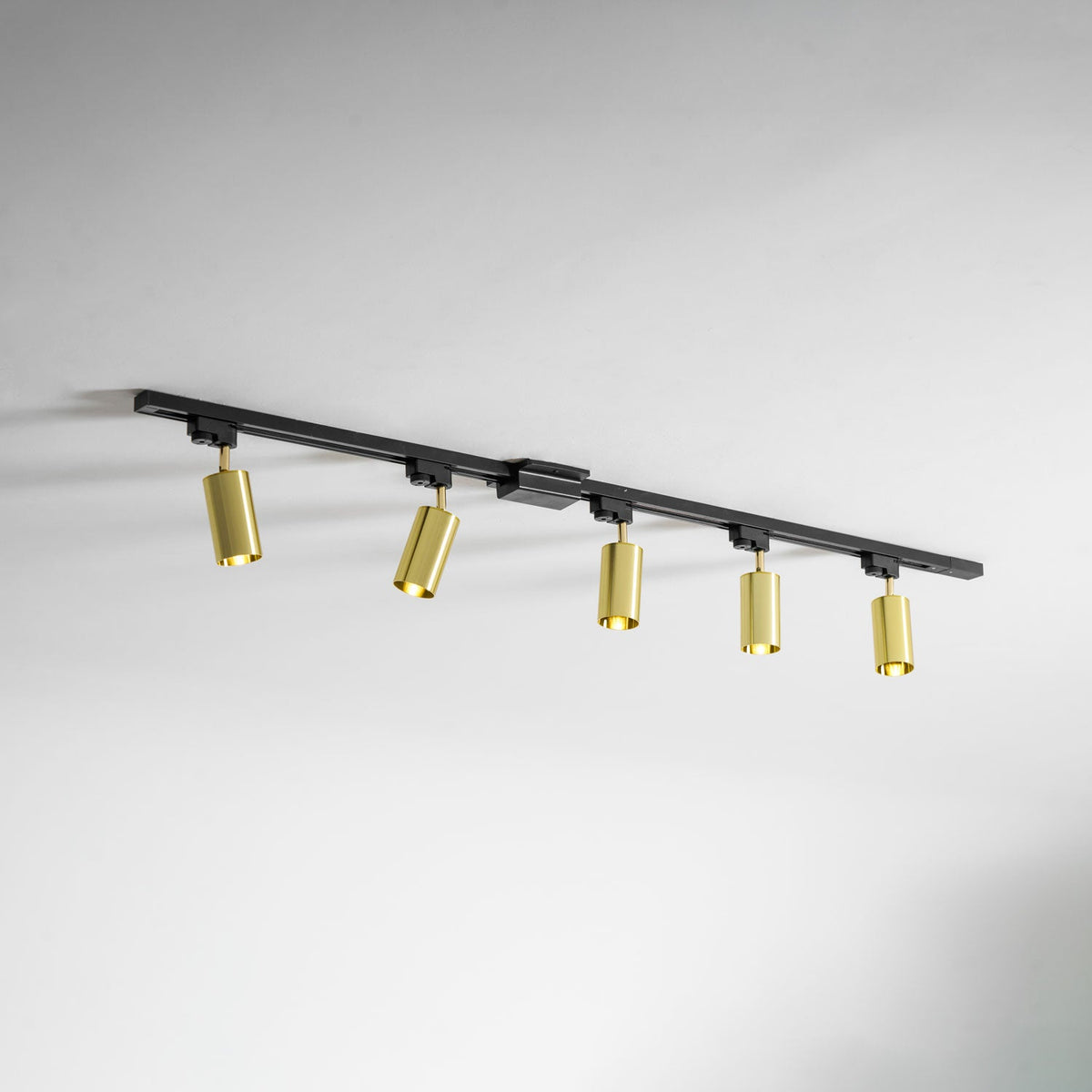 Five gold Clérachic spotlights on a black track, seen at an angle along a white wall and ceiling.