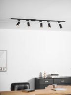 Clérachic track with five black cylindrical spotlights, above a white wall, a black chest of drawers and a desk.