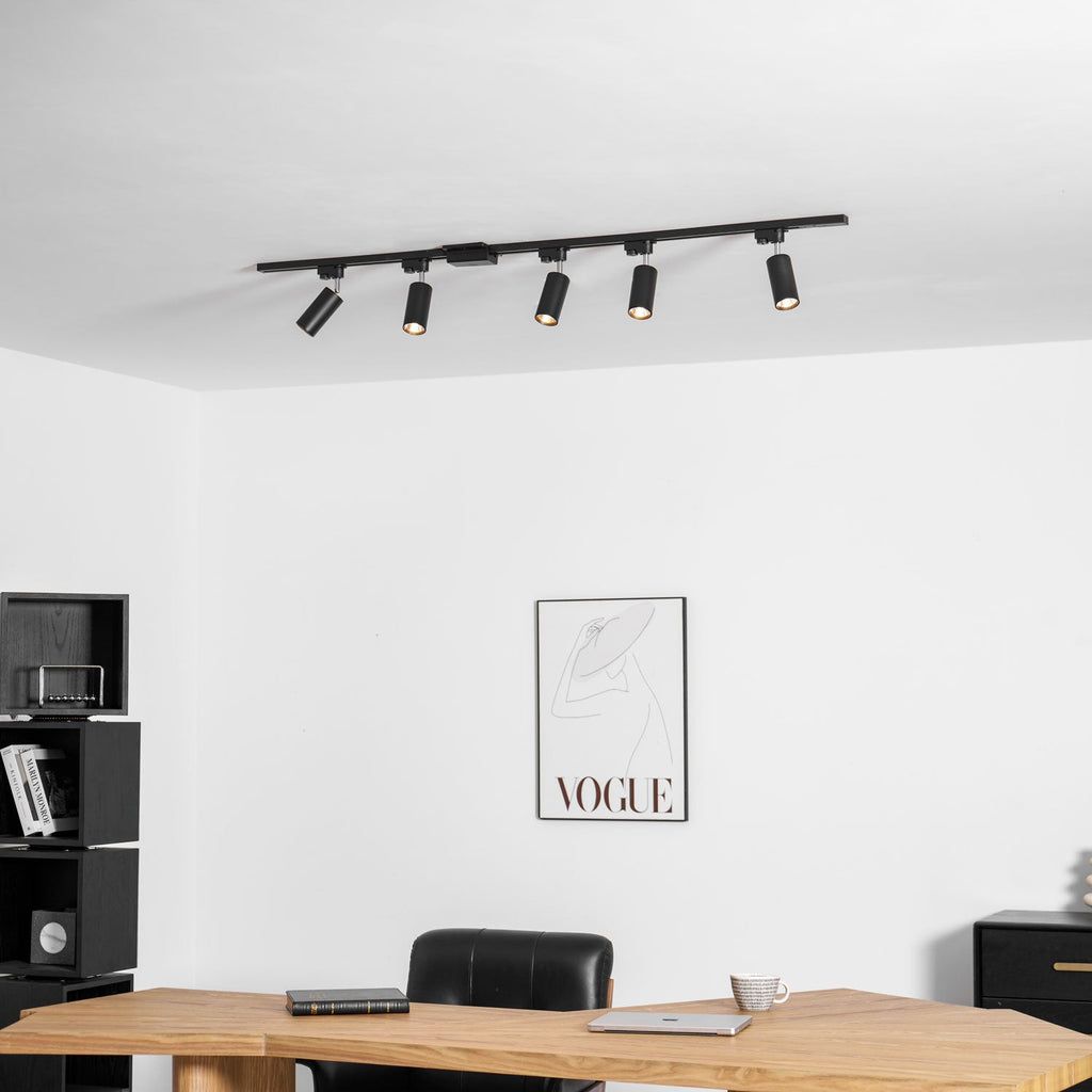 Five black Clérachic spotlights along a black track above a desk and black shelving, with a framed line-drawing print.
