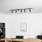 Five black Clérachic spotlights along a black track above a desk and black shelving, with a framed line-drawing print.