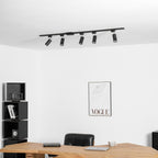 Clérachic black track with five black heads at the ceiling, above a white wall with a framed print and a desk.