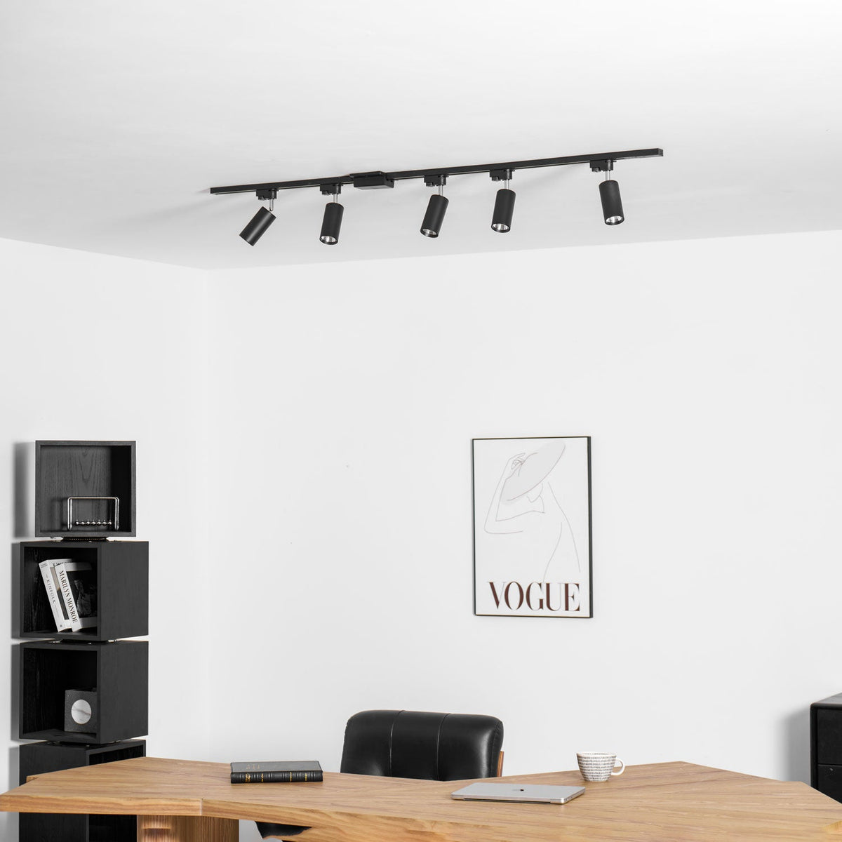 Clérachic black track with five black heads at the ceiling, above a white wall with a framed print and a desk.