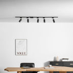Five black Clérachic track spotlights above a white wall with a framed print, a desk and a black chest.