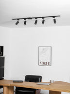 Clérachic black track light with five black cylindrical heads near the ceiling, above a wooden desk and a framed print.