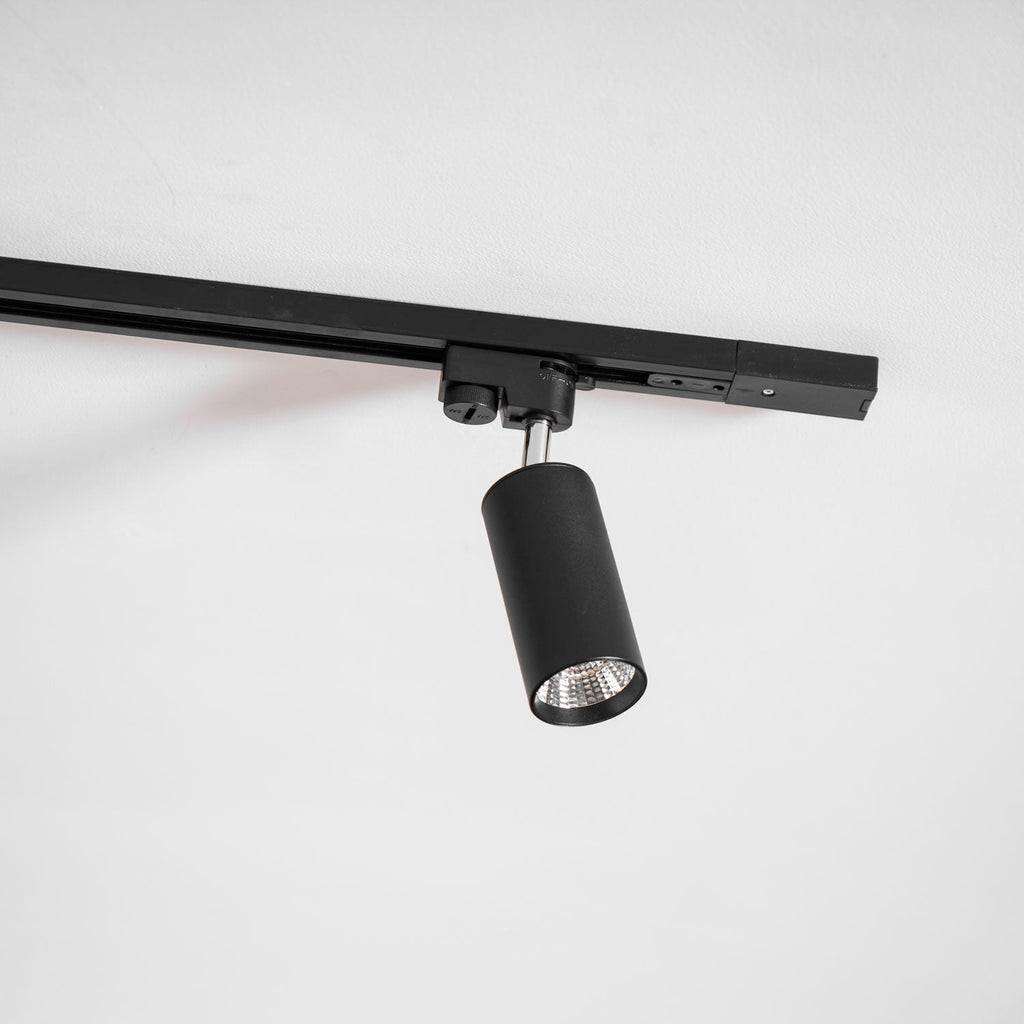 Close view of a black cylindrical Clérachic track spotlight with its adaptor, hanging from a black rail.