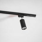 Close view of a black cylindrical Clérachic track spotlight with its adaptor, hanging from a black rail.