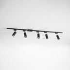 Five black cylindrical Clérachic spotlights on a long black track, hung at an angle against a pale grey wall.