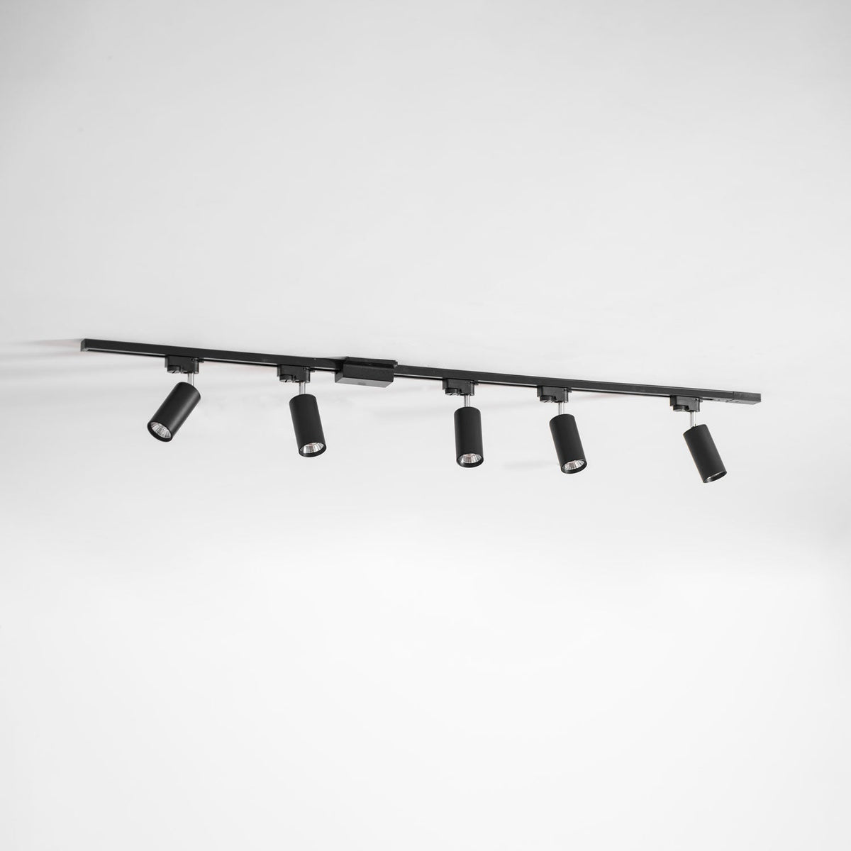 Five black cylindrical Clérachic spotlights on a long black track, hung at an angle against a pale grey wall.