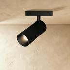 Clérachic matte black track spotlight head swivelled on its ceiling rail mount, beaming warm light forward.