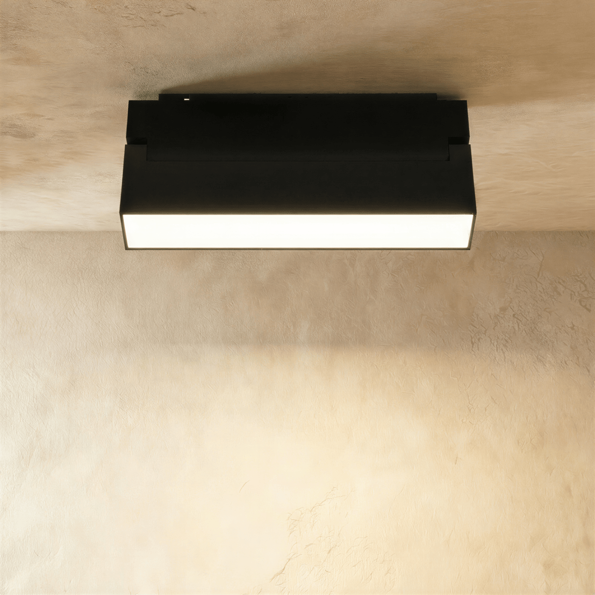 Clérachic black surface-mount linear floodlight glowing along its frosted lens, fixed to an overhead track rail.